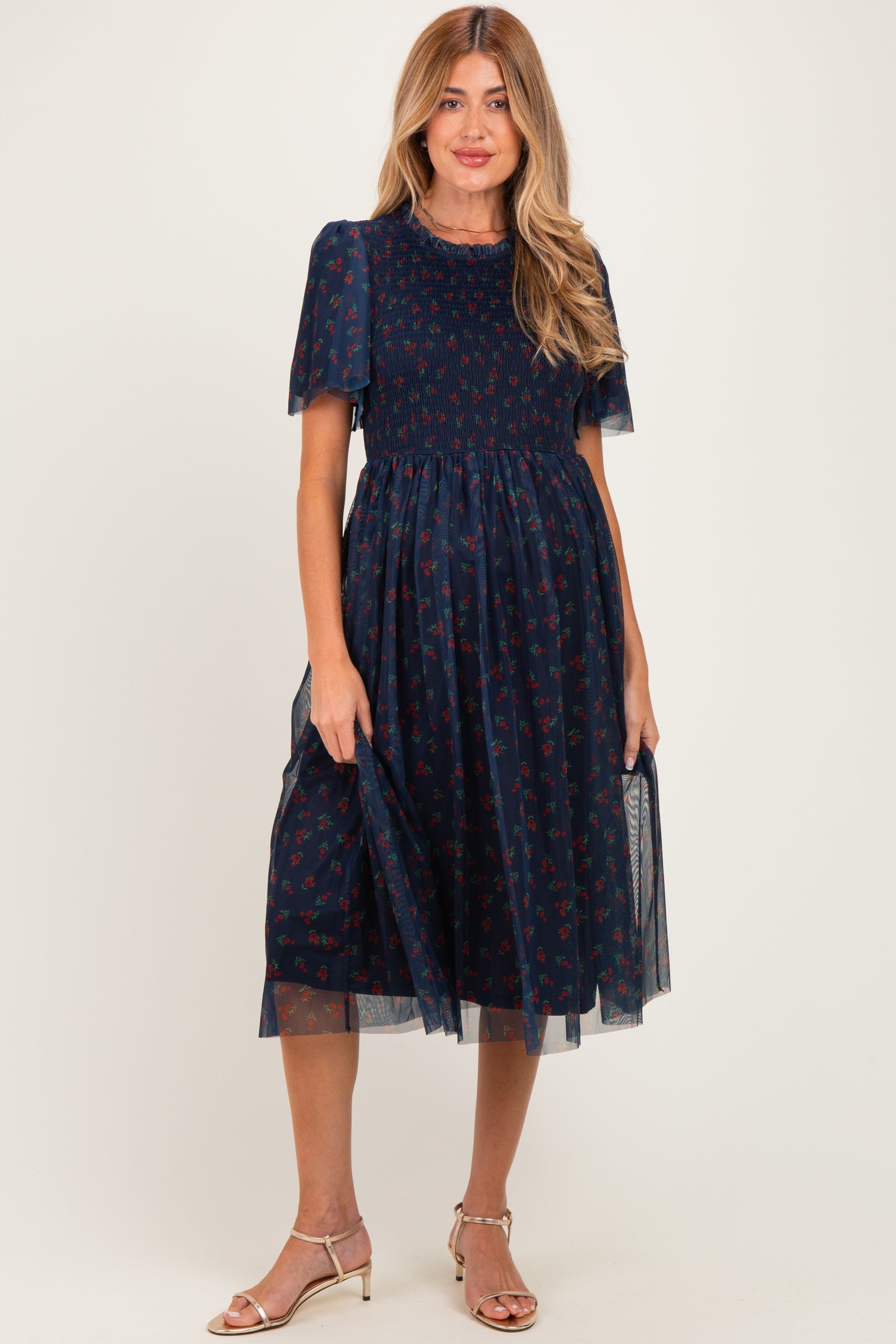 woman wearing a navy maternity dress with floral print and sheer puff sleeves, holding the skirt to show off the baby bump