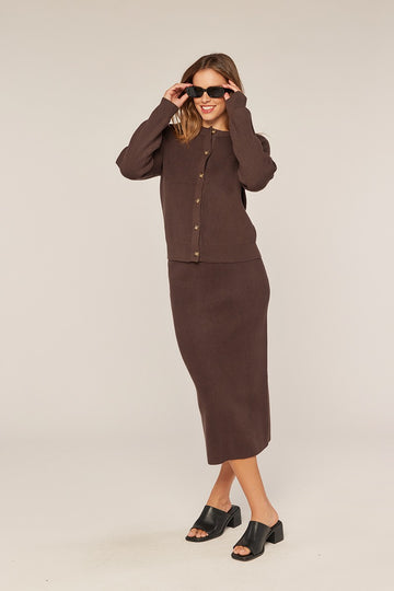 woman wearing a dark brown long sleeve cardigan and matching midi skirt with buttons, styled with sunglasses and mules