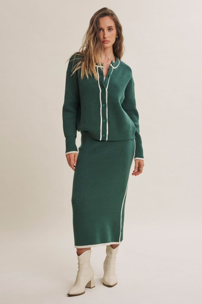 woman wearing a dark green cardigan and matching skirt with white trim and heeled boots