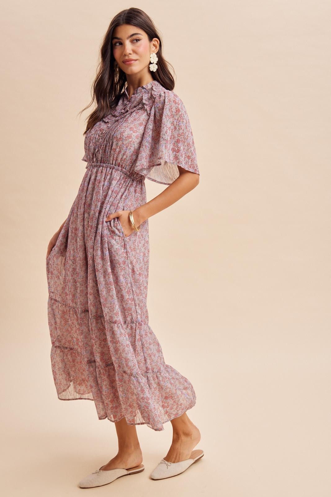 woman wearing a floral maxi dress with short sleeves and tiered skirt, standing in profile against a light background