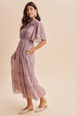 woman wearing a floral maxi dress with short sleeves and tiered skirt, standing in profile against a light background