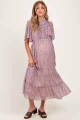 woman wearing a lavender floral maternity dress with a ruffled neckline and flowing sleeves, showcasing her baby bump
