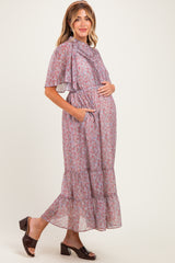 woman wearing a lavender floral maxi maternity dress with short sleeves and pockets, holding her baby bump