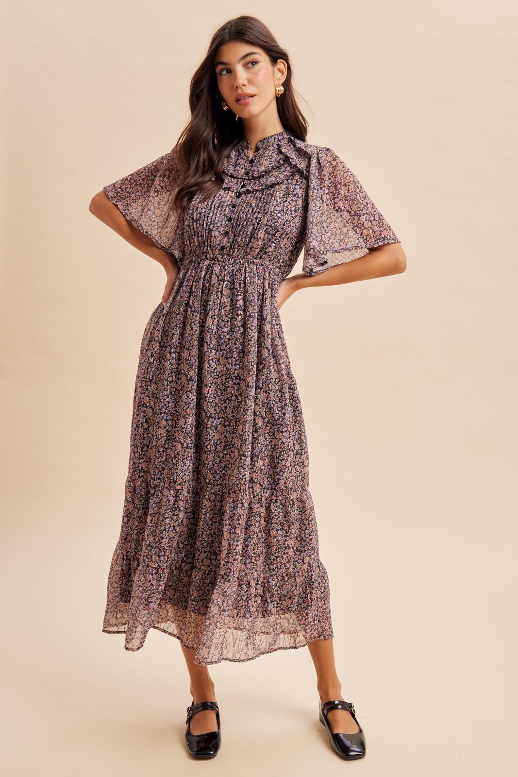 woman wearing a floral midi dress with short sleeves and a tied collar detail, posing with hands on hips