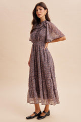 woman wearing a floral print maxi dress with flutter sleeves and a cinched waist, paired with black flats