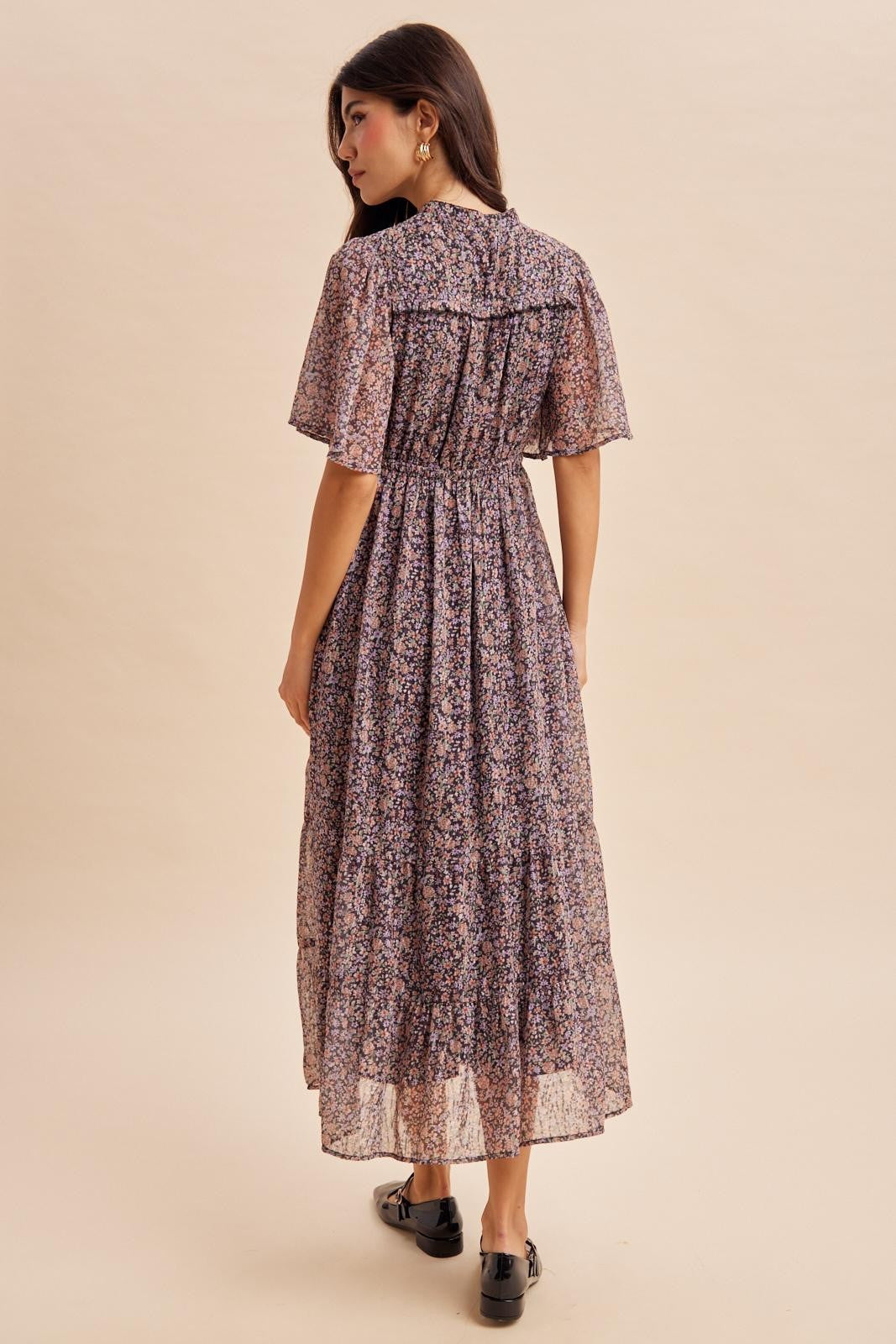 woman wearing a back view of a floral print maxi dress with puff sleeves and a flowy skirt