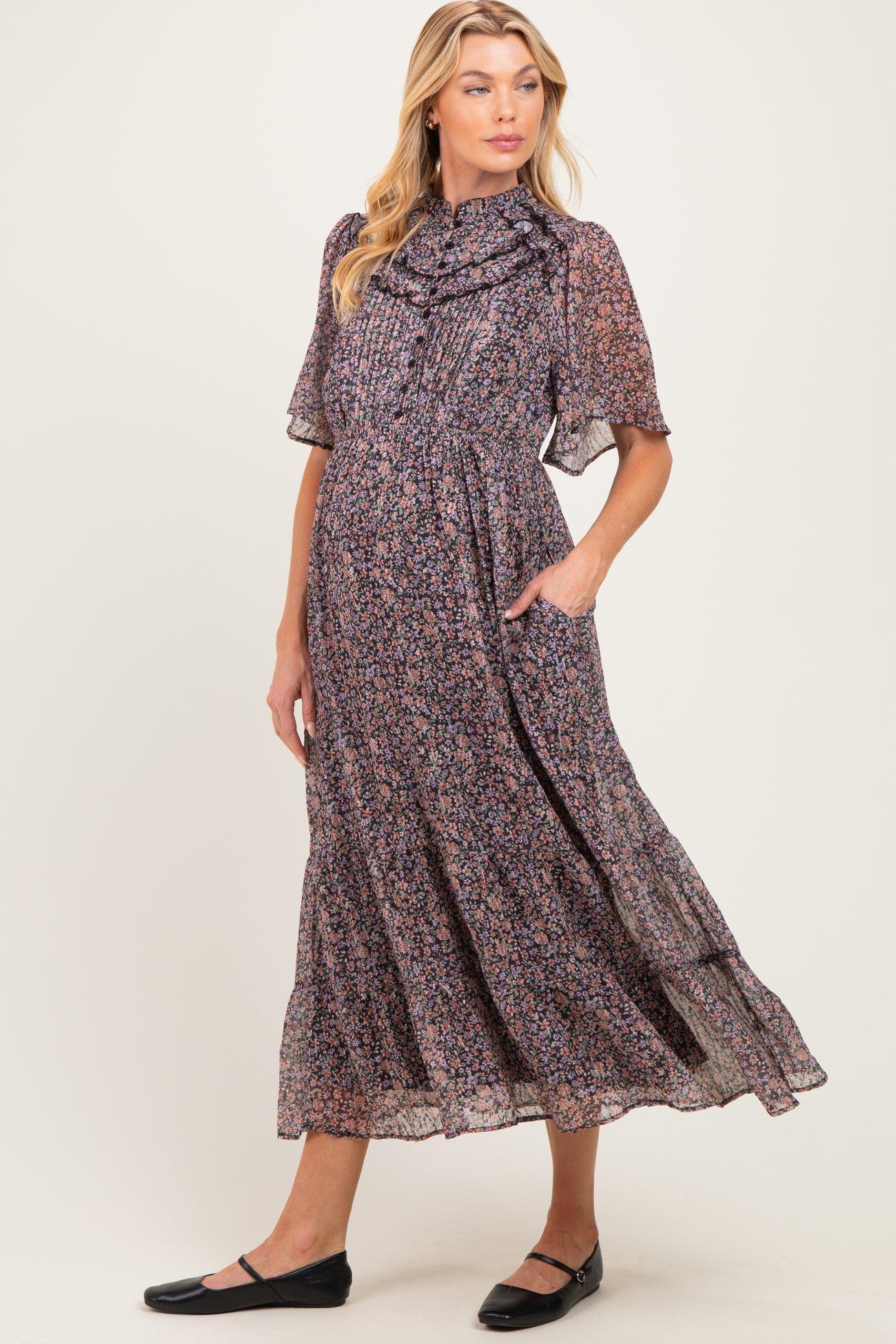 woman wearing a floral print maternity dress with short sleeves and a ruffled neckline, featuring pockets and a flowing skirt