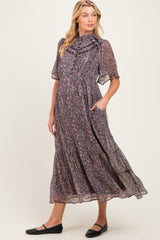 woman wearing a floral print maternity dress with short sleeves and a ruffled neckline, featuring pockets and a flowing skirt