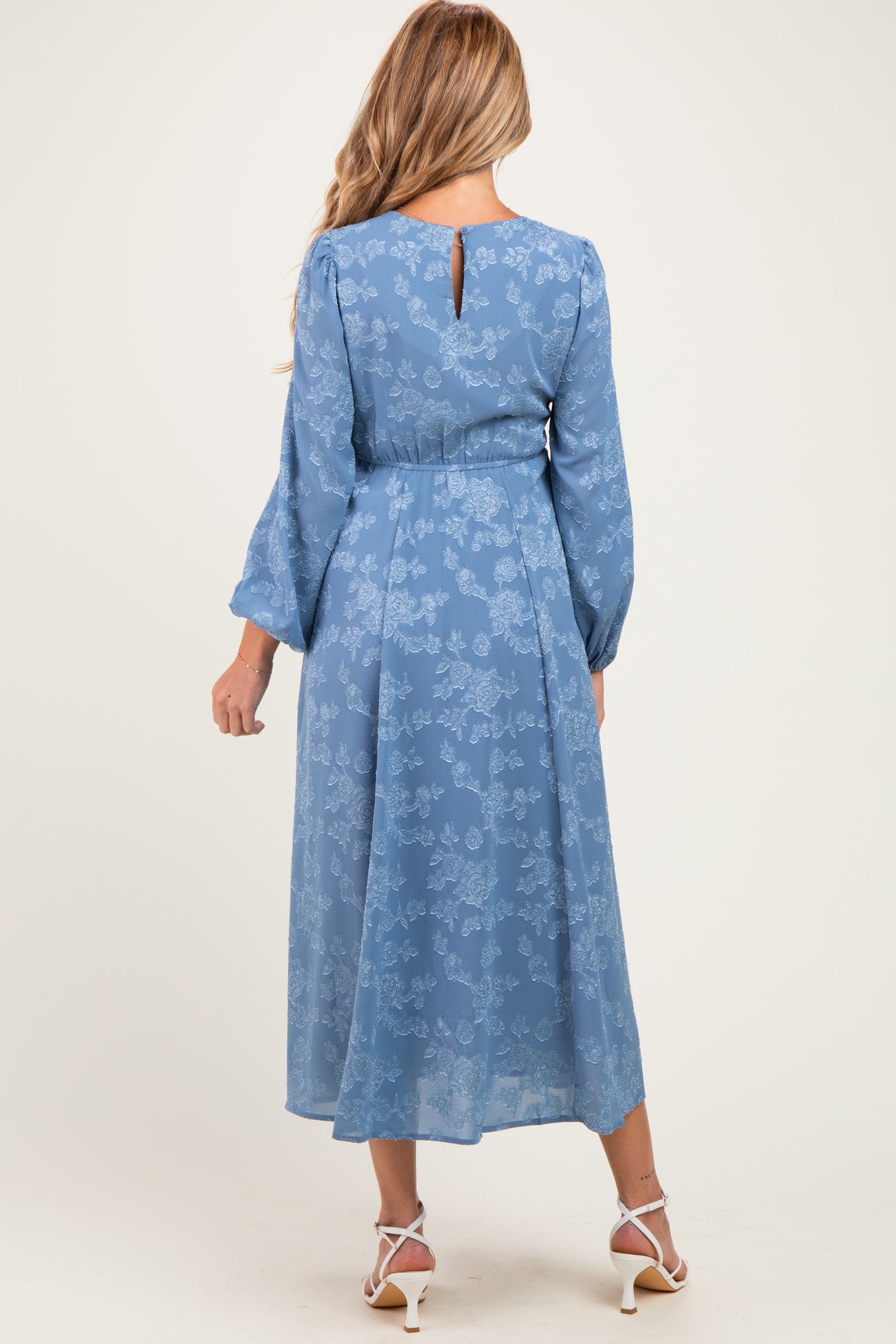 woman wearing a blue floral maternity dress with long sleeves and a keyhole back detail, showcasing her baby bump
