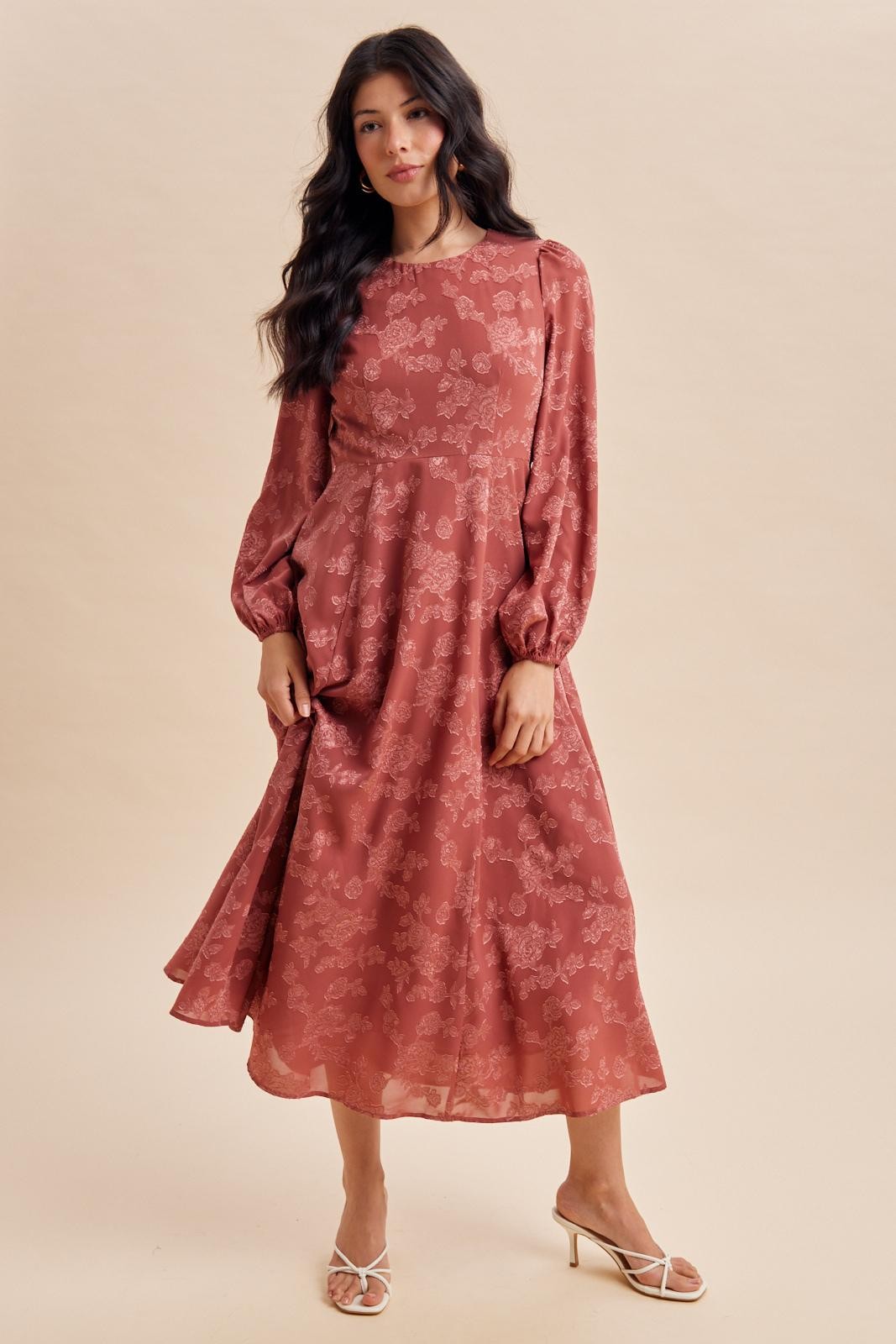 woman wearing a rust colored floral midi dress with puff sleeves and a flowy silhouette