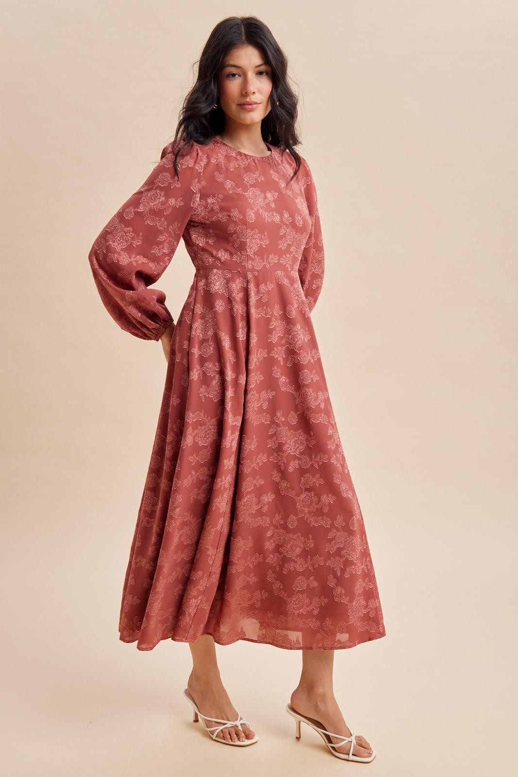 woman wearing a rust-colored long sleeve floral maxi dress with a fitted waist and flowy skirt
