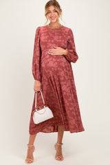 woman wearing a rust floral long sleeve maternity dress and holding her baby bump with a white handbag