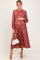 woman wearing a rust floral long sleeve maternity dress and holding her baby bump with a white handbag