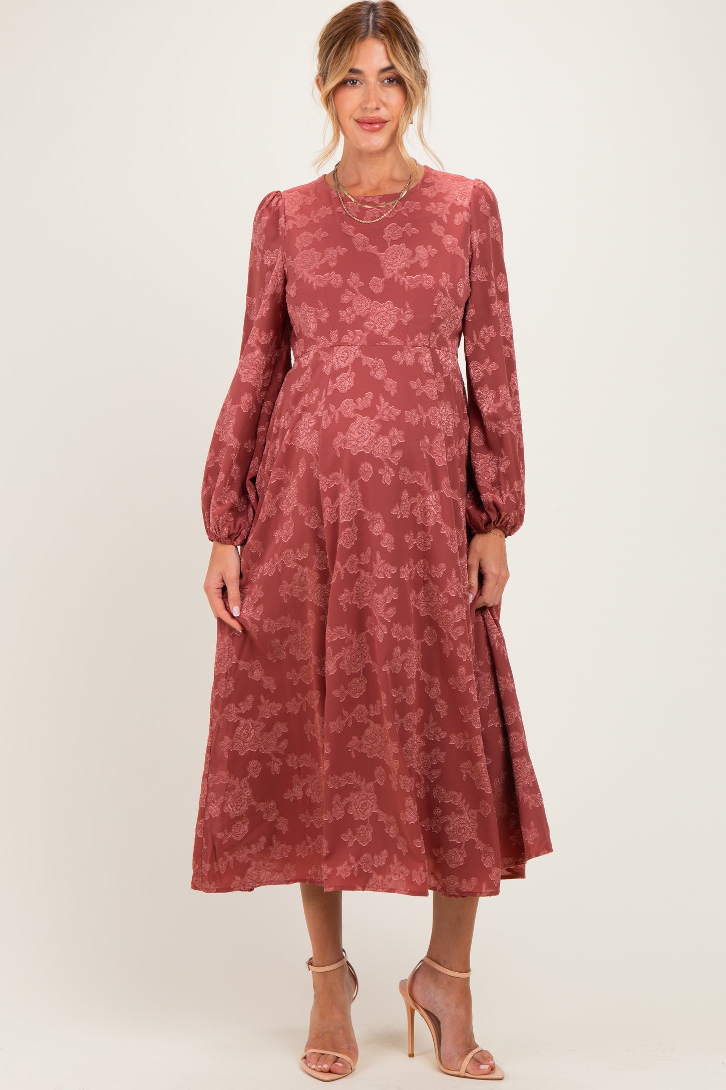 woman wearing a rose patterned maternity dress with long sleeves and a flowing skirt, showing her baby bump