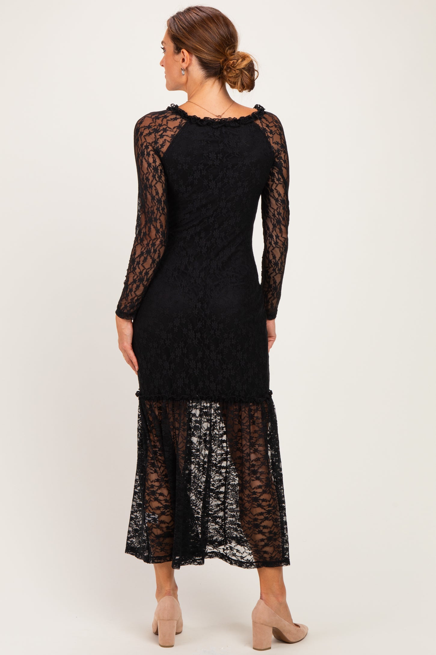woman wearing a black long sleeve lace dress with a tiered hem and transparent details, viewed from the back