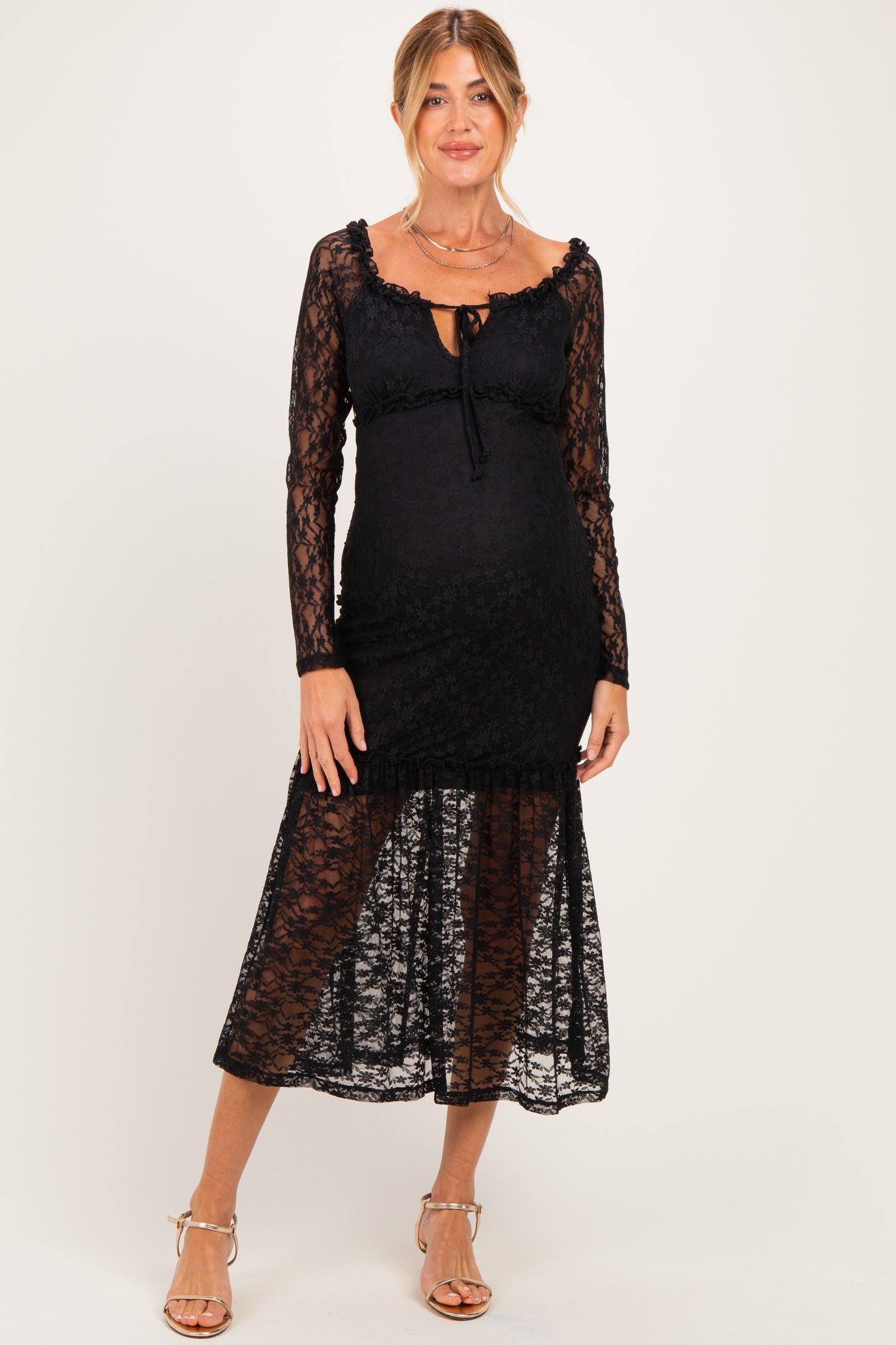 woman wearing a black lace maternity dress with long sleeves and a tiered skirt, showcasing a baby bump