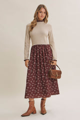woman wearing a beige long sleeve knit top and a burgundy floral midi skirt, holding a brown handbag