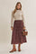 woman wearing a beige long sleeve knit top and a burgundy floral midi skirt, holding a brown handbag