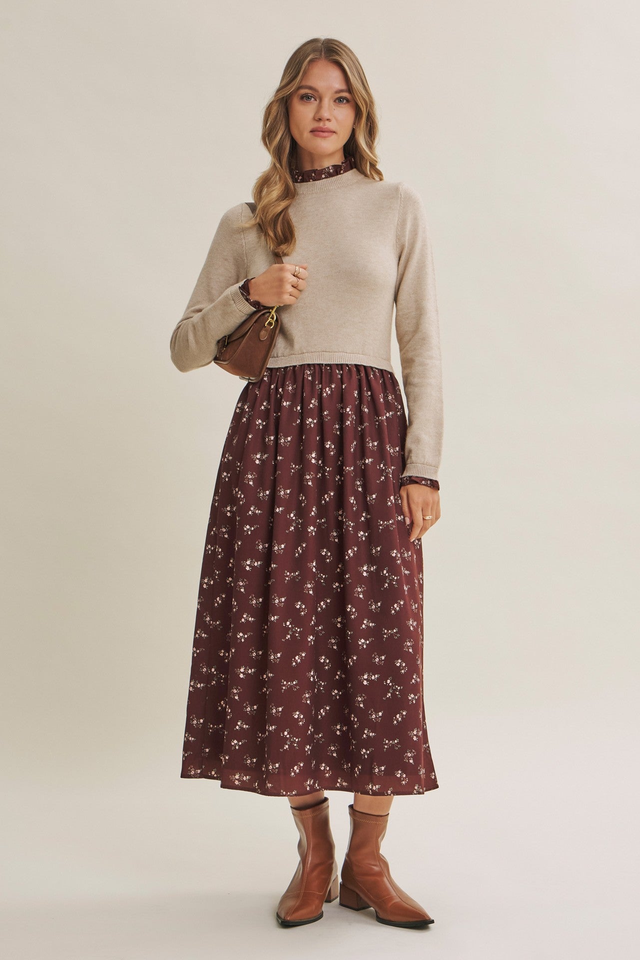 woman wearing a beige sweater top with a maroon floral midi skirt, accessorized with a small handbag and brown ankle boots
