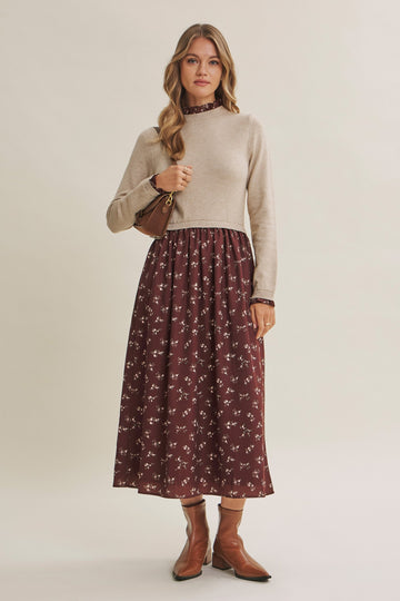 woman wearing a beige sweater top with a maroon floral midi skirt, accessorized with a small handbag and brown ankle boots