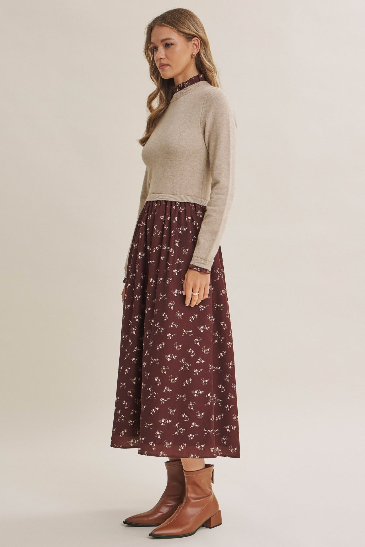 woman wearing a beige cropped sweater with a burgundy floral maxi dress and brown ankle boots