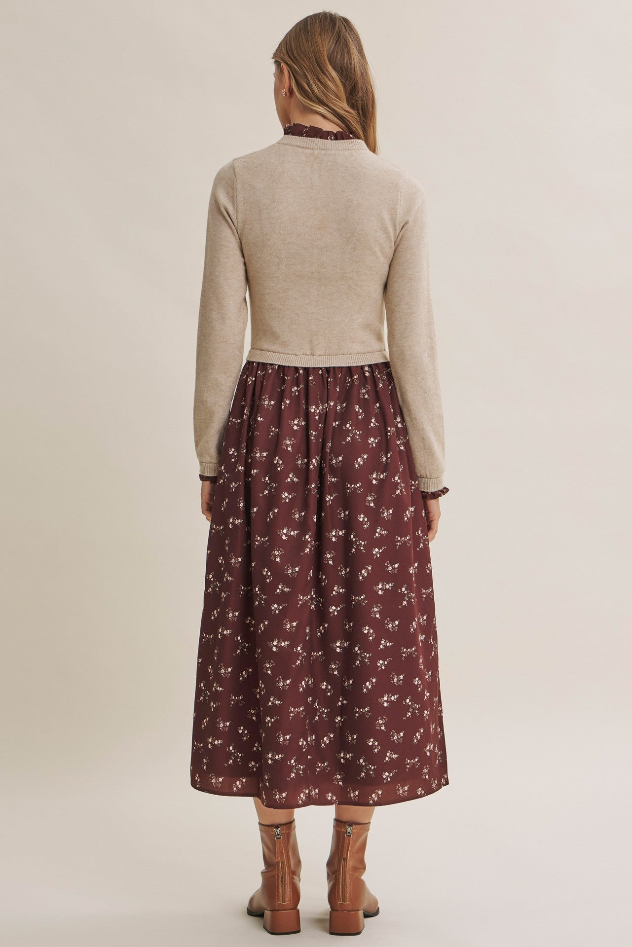 woman wearing a beige long sleeve sweater over a burgundy floral maxi dress, viewed from the back