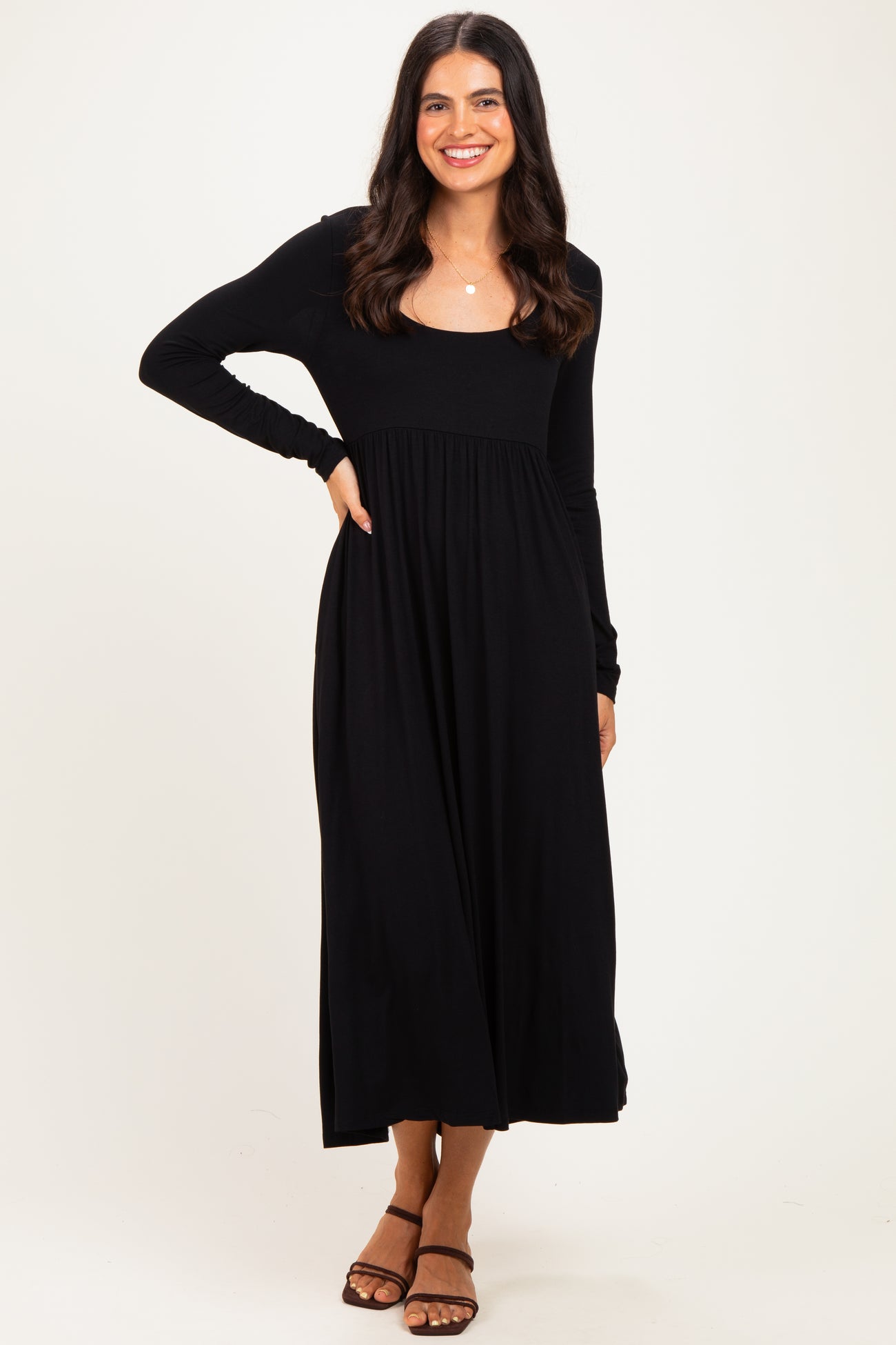 woman wearing a black long sleeve maxi dress with a fitted bodice and flowing skirt, standing and smiling