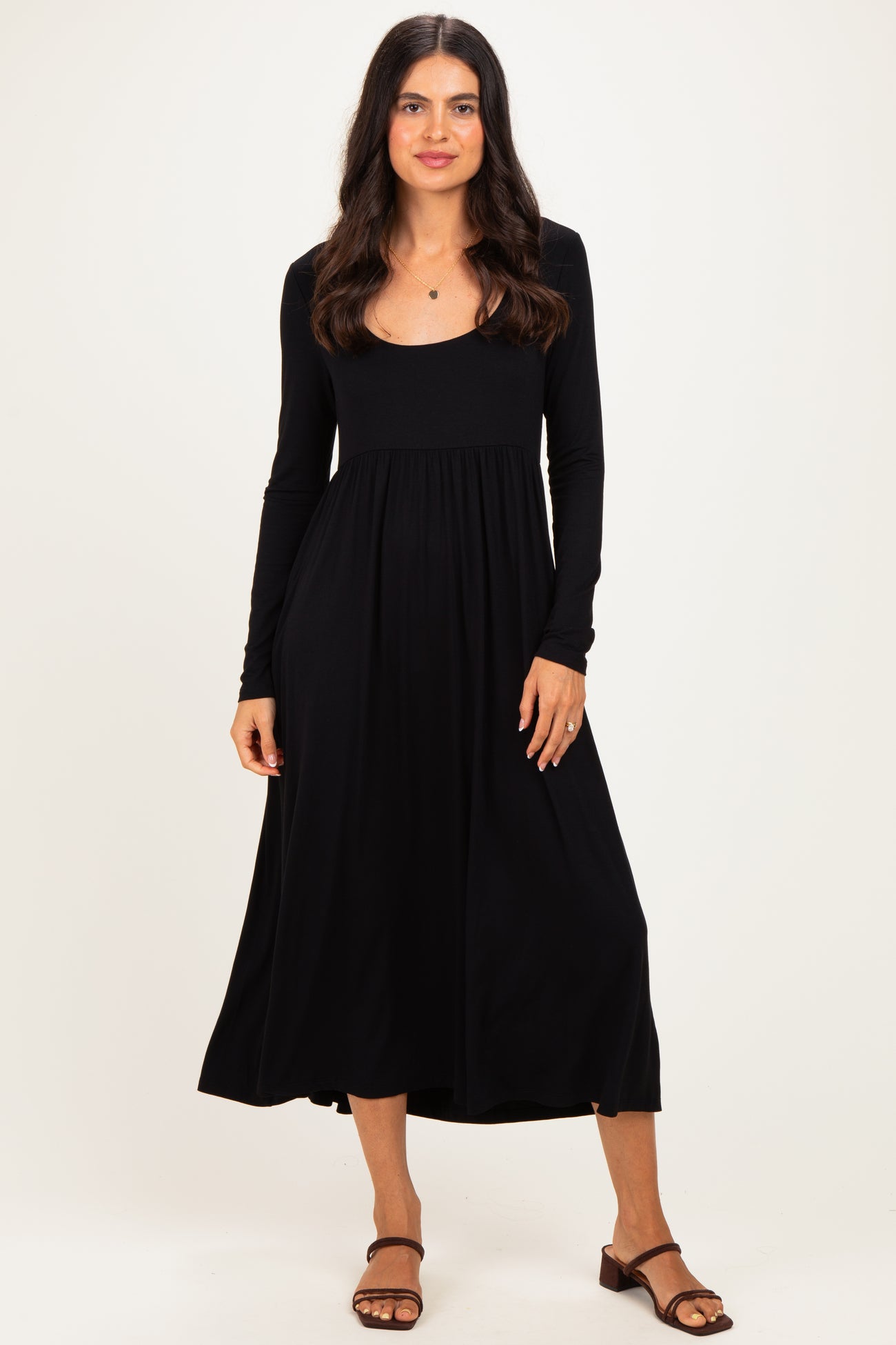 woman wearing a black long sleeve midi dress with a fitted bodice and flowing skirt, standing on a plain background