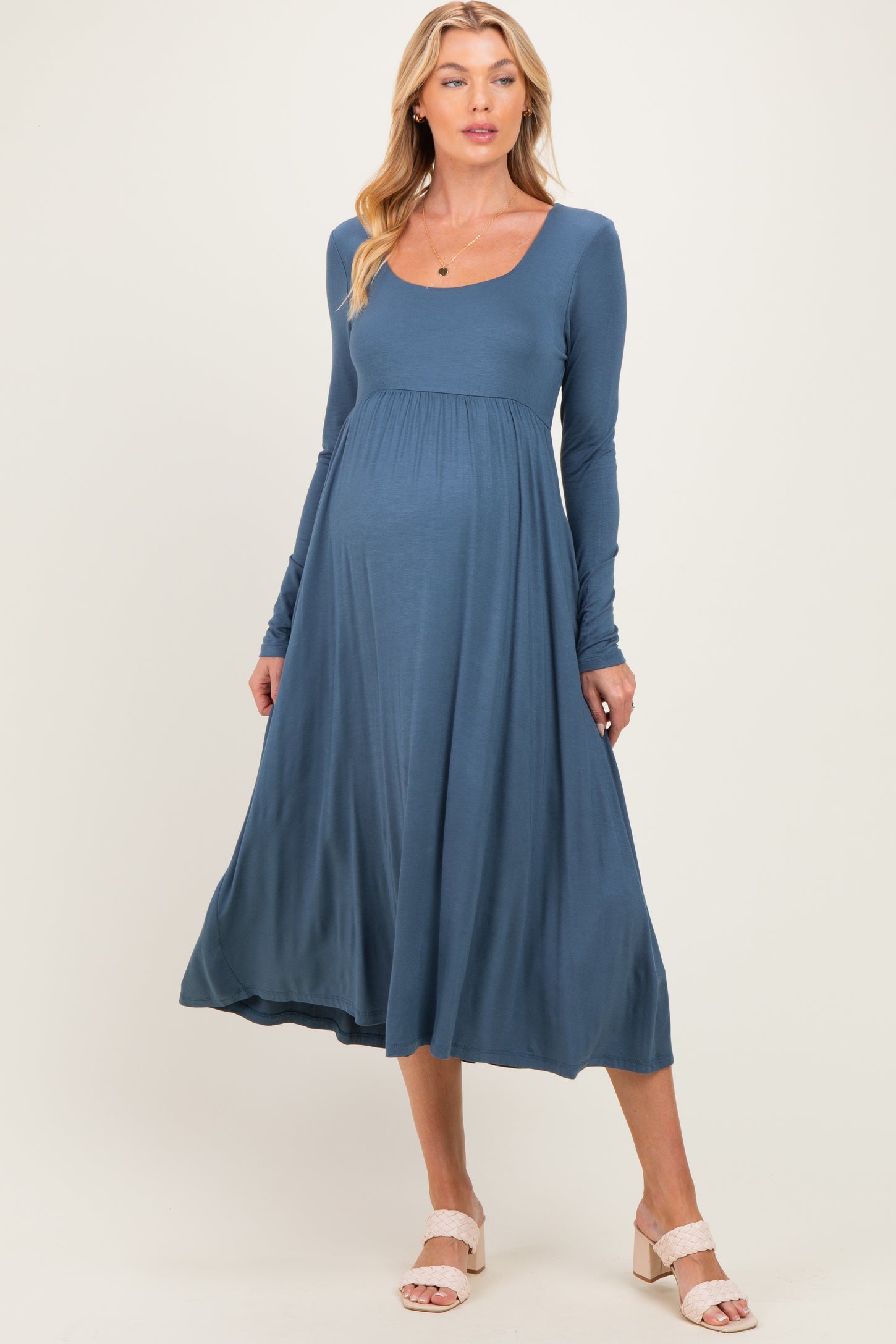 woman wearing a blue long sleeve maternity dress with a scoop neckline and flowing skirt, showing a baby bump