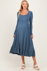 woman wearing a blue long sleeve maternity dress with a scoop neckline and flowing skirt, showing a baby bump