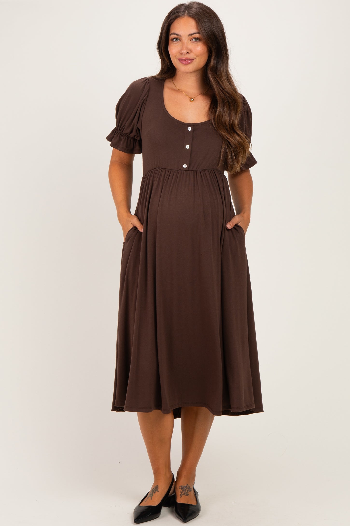 woman wearing a brown puff sleeve maternity dress with buttons and pockets, showcasing her baby bump