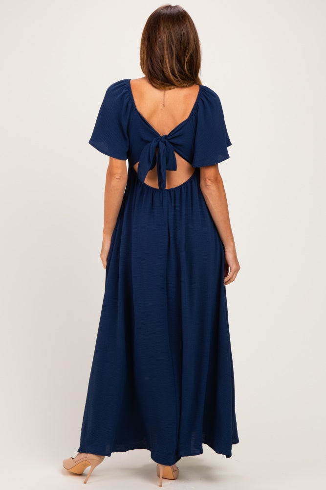 woman wearing a dark navy blue maxi dress with a tied open back and flutter sleeves