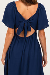 back view of a woman wearing a navy blue dress with short flutter sleeves and a tied open back detail