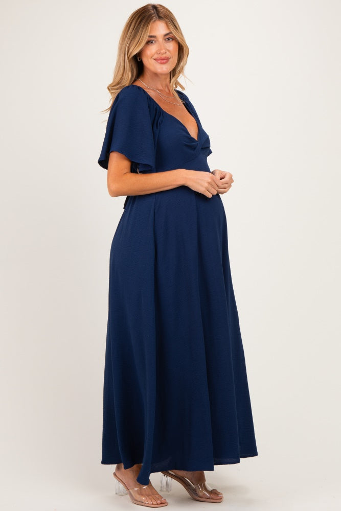 woman wearing a navy blue maxi maternity dress with short flutter sleeves and a v-neck, showing her baby bump