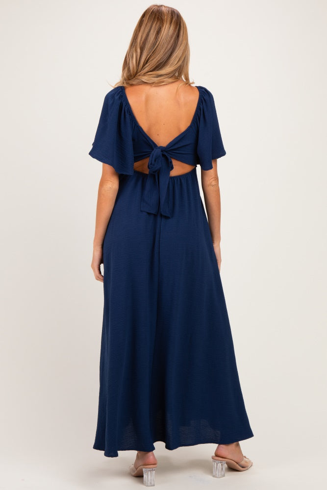 woman wearing a navy blue maternity maxi dress with a tie-back detail and short sleeves, showing a stylish open back