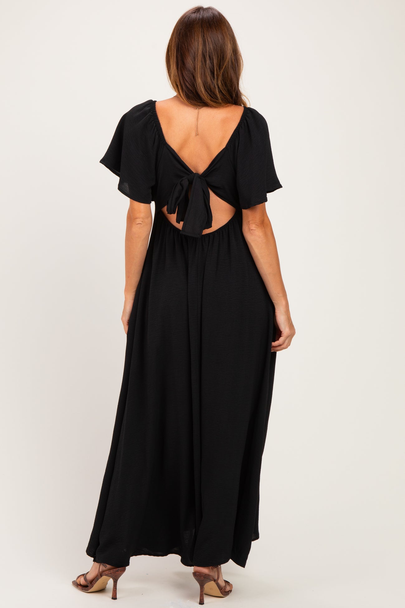 woman wearing a black maxi dress with short flutter sleeves and a tie-back detail