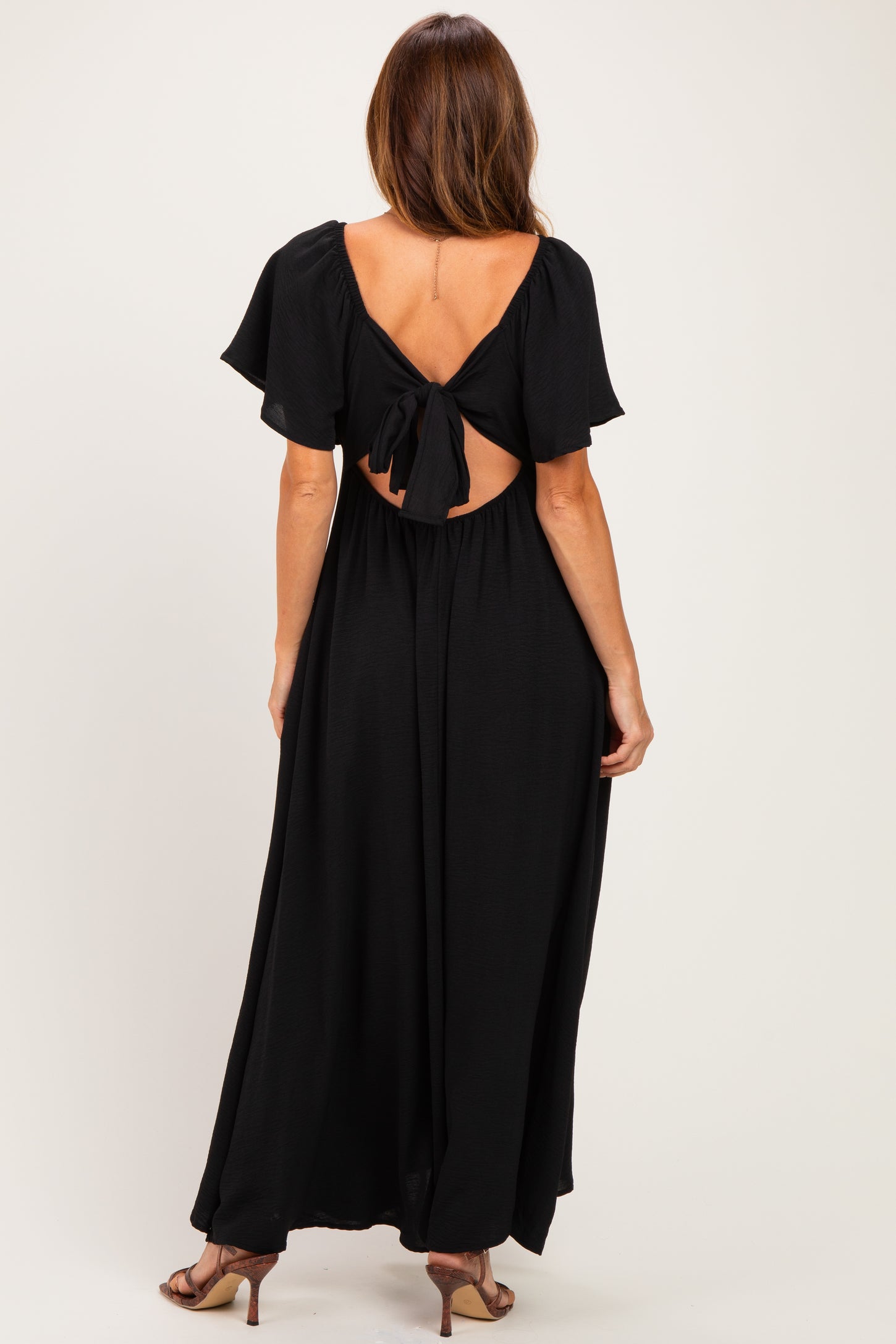 woman wearing a black maxi dress with short flutter sleeves and a tie-back detail