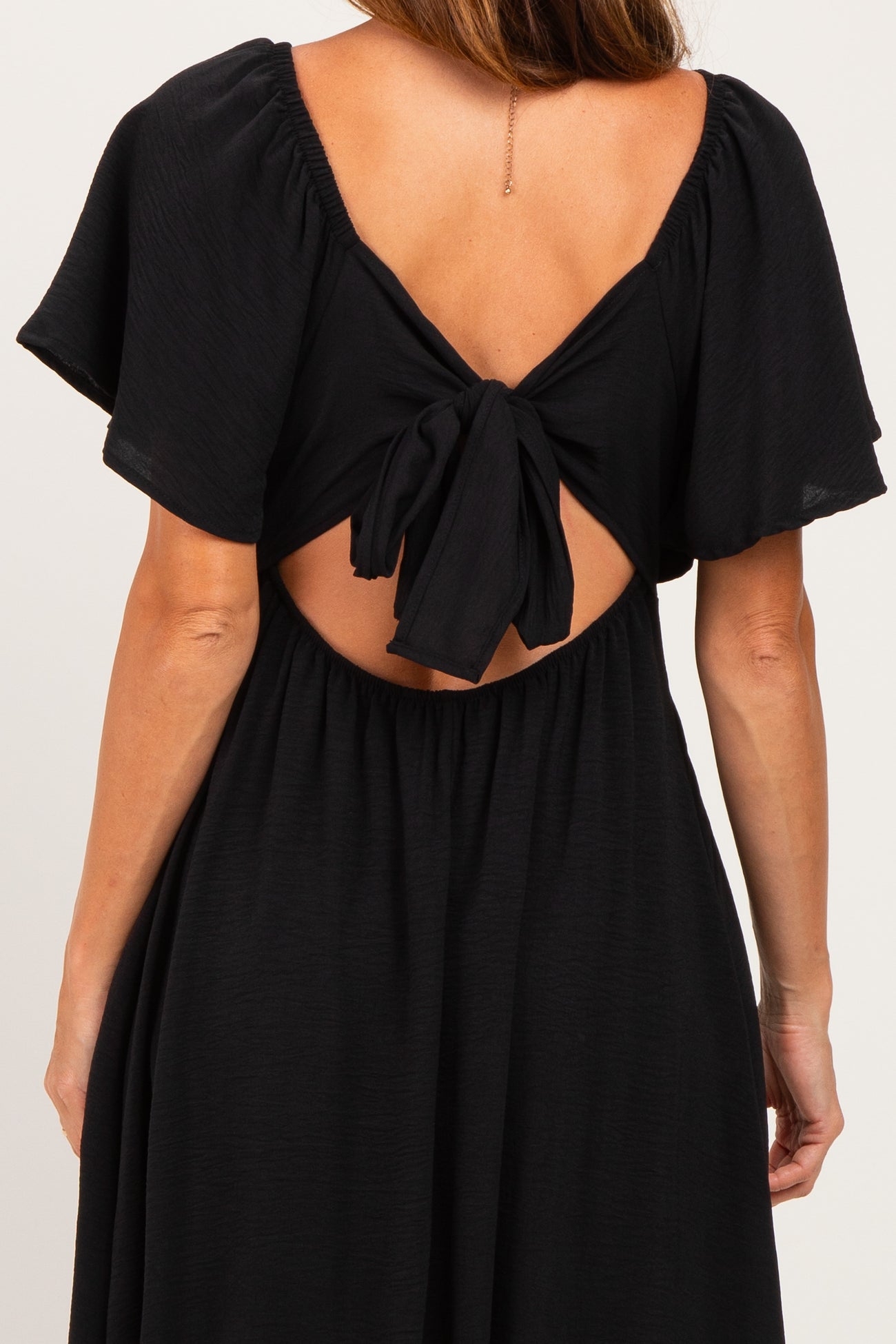 woman wearing a black backless dress with short flutter sleeves and a tied bow detail at the back