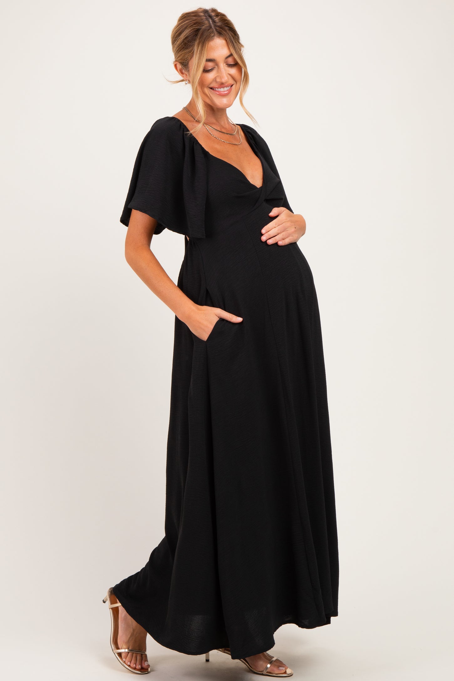 woman wearing a black maternity maxi dress with short sleeves and pockets, showcasing her baby bump