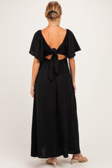 woman wearing a black maxi maternity dress with short flutter sleeves and a tie-back detail