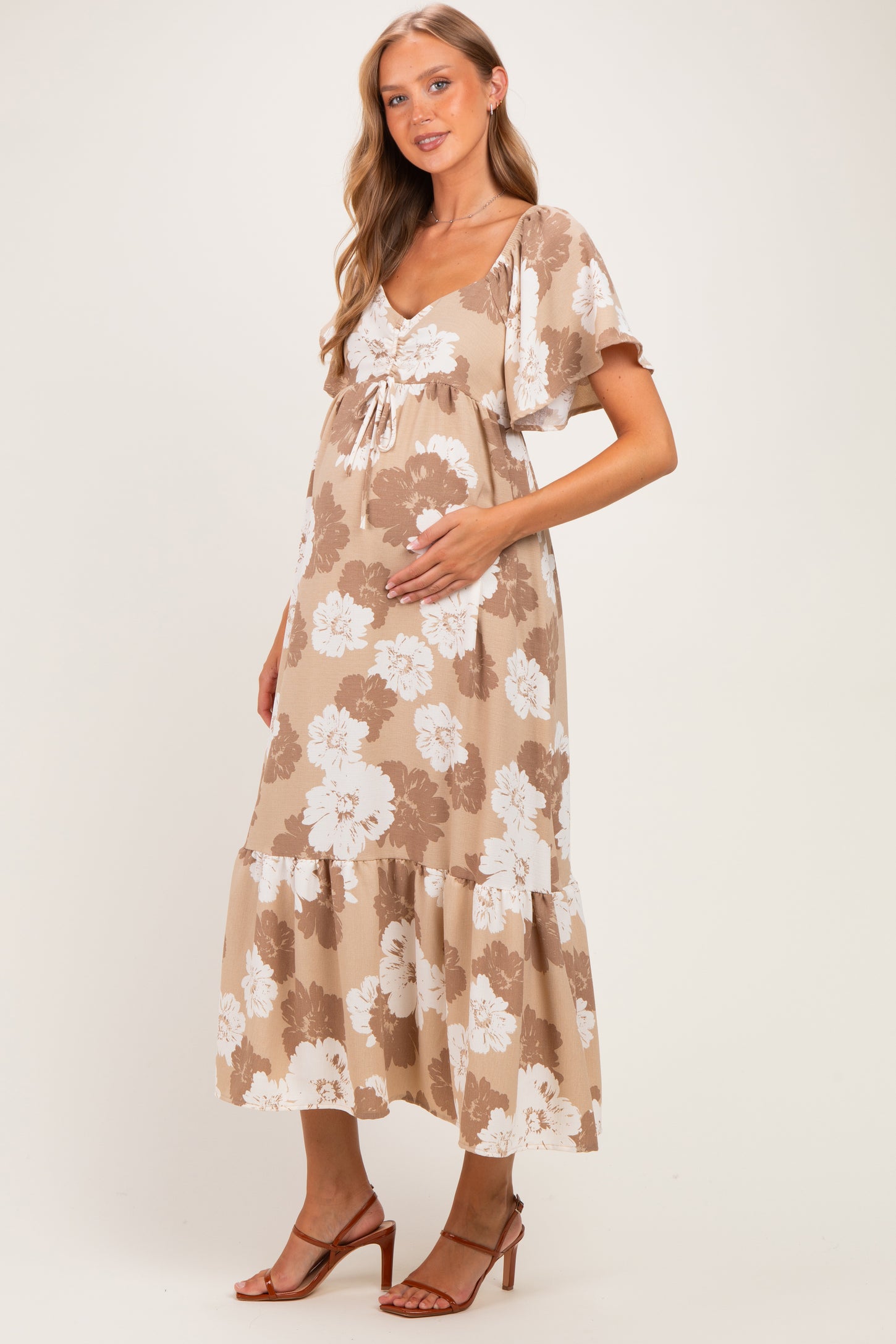 woman wearing a floral beige maternity dress with a tiered skirt and holding her baby bump