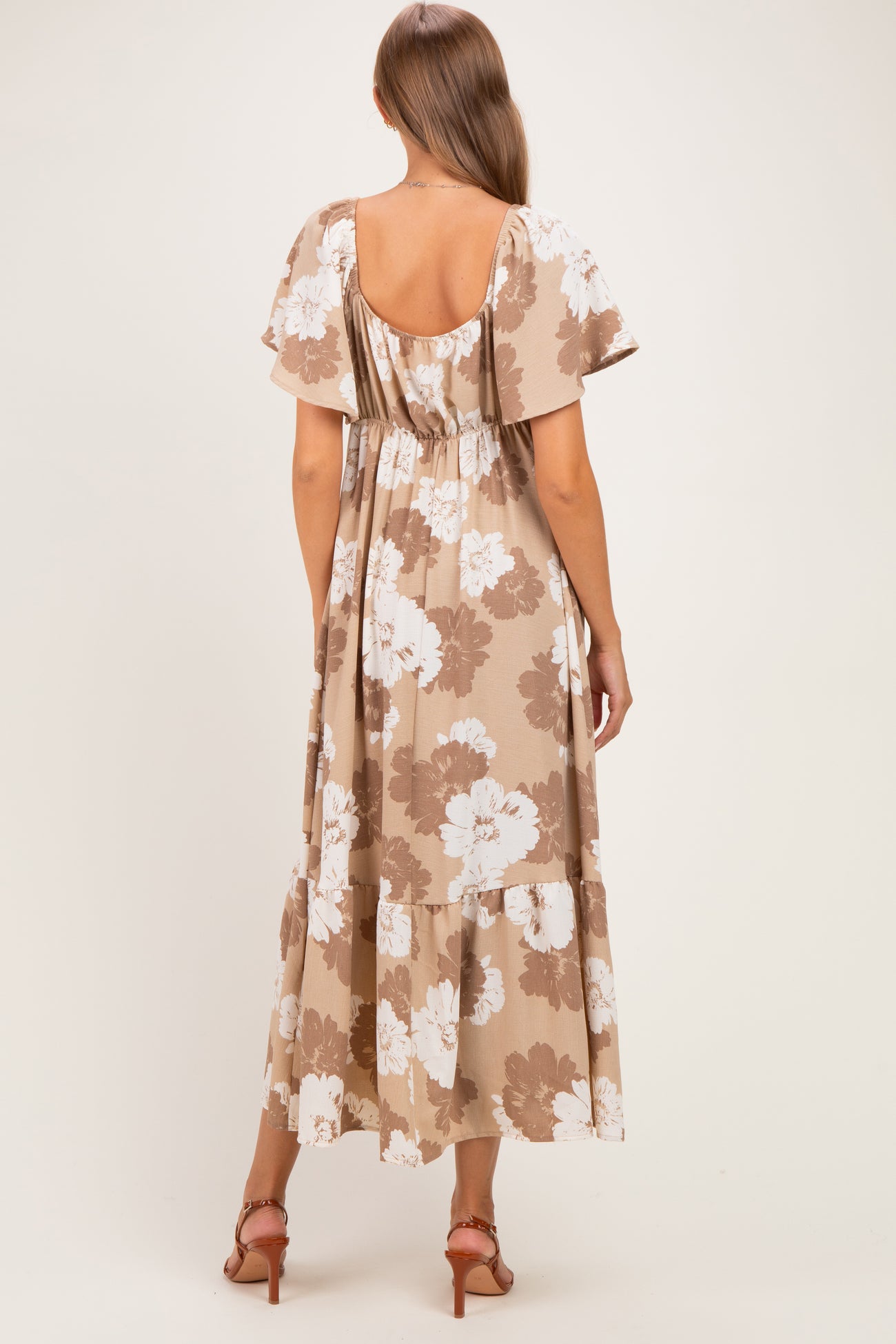 woman wearing a brown floral maternity maxi dress with flutter sleeves and a tiered hem, showing her baby bump from the back