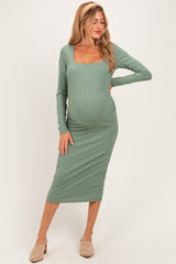 woman wearing a sage green maternity midi dress with long sleeves and a square neckline, highlighting her baby bump