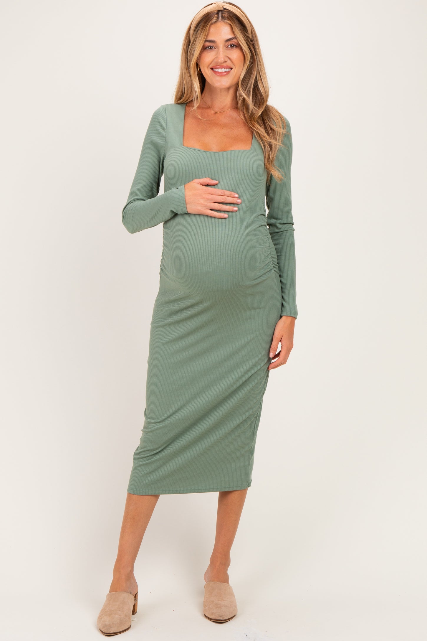 woman wearing a fitted sage green long sleeve maternity dress with a square neckline and holding her baby bump