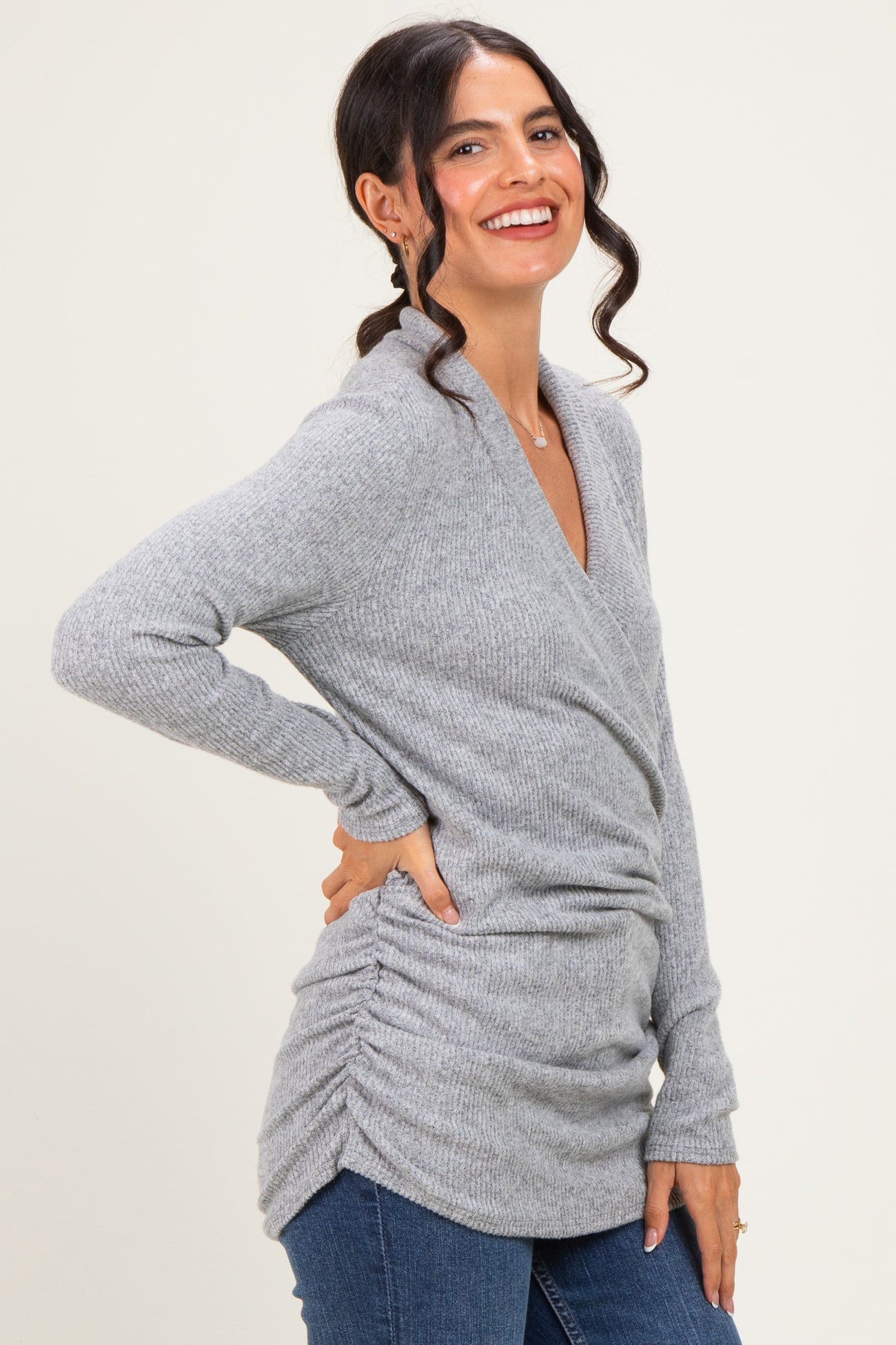 woman wearing a gray long sleeve wrap sweater with side ruching and smiling at the camera