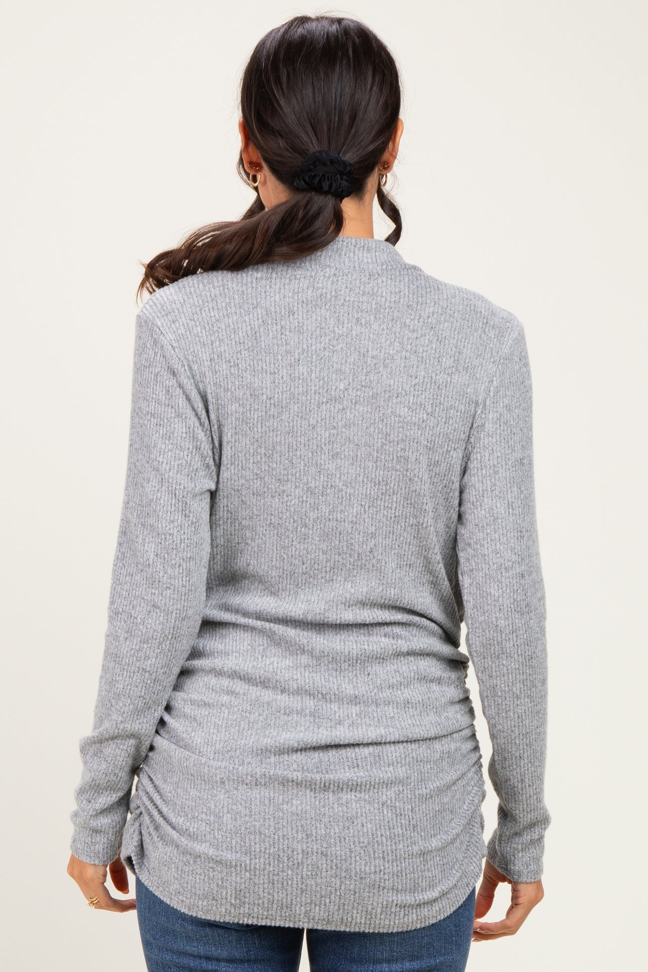 woman wearing a gray long sleeve ribbed sweater with gathered side details, viewed from the back
