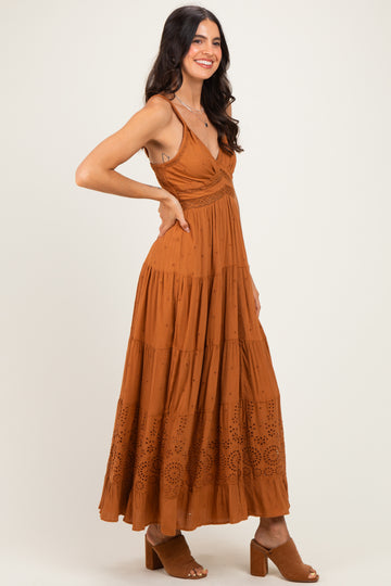woman wearing a rust-colored maxi dress with a tiered design and eyelet details, paired with brown block-heel sandals