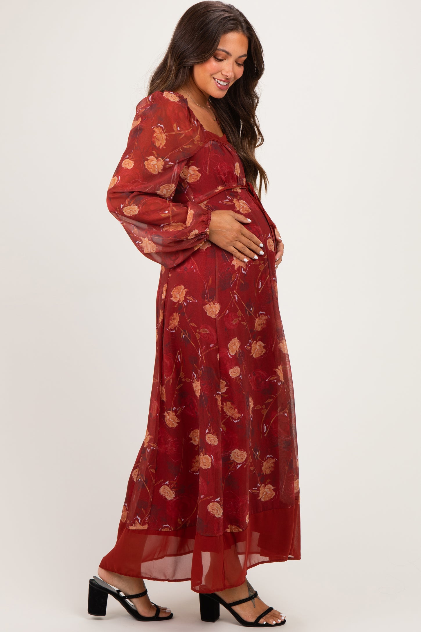 woman wearing a flowy red floral maternity maxi dress and holding her baby bump