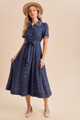 woman wearing a navy blue short sleeve button-up dress with floral print and a tie waist, paired with a beige hat