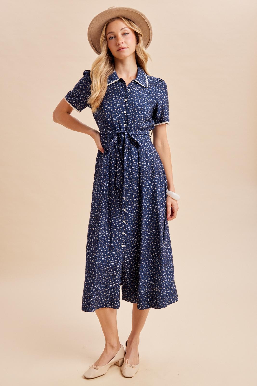 woman wearing a navy blue button-up midi dress with a tie waist and floral print, styled with a wide-brimmed hat